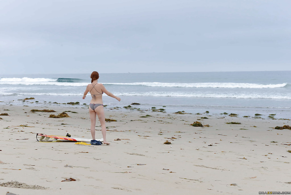 Рыжая серфингистка позирует в купальнике на берегу океана 2 фотография