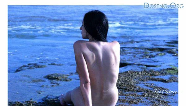 Длинноволосая брюнетка позирует голышом на морском берегу 10 фотография