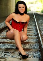 Брюнетка в ошейнике позирует на железной дороге в красном корсете и трусах 3 фото