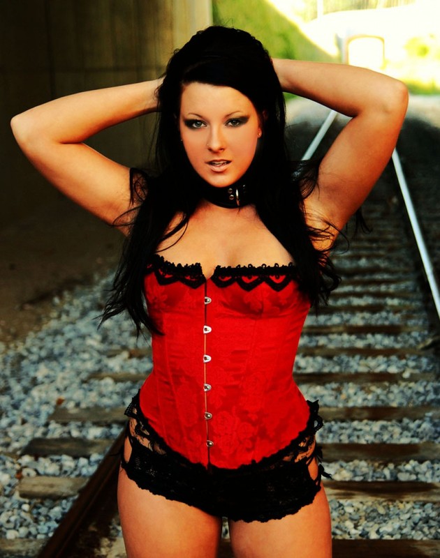 Брюнетка в ошейнике позирует на железной дороге в красном корсете и трусах 4 фотография