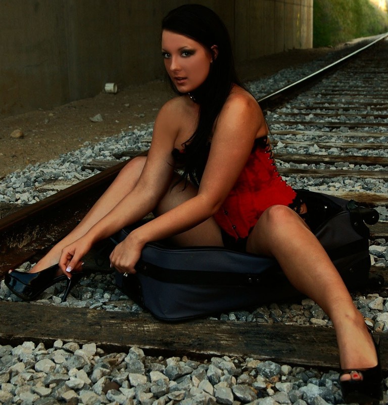 Брюнетка в ошейнике позирует на железной дороге в красном корсете и трусах 8 фотография