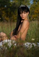 Длинноволосая брюнетка в диадеме светит голым телом в высокой траве 5 фотография